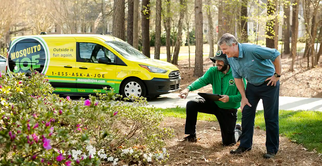 A Mosquito Joe employee pointing at plants with a customer in front of a van.