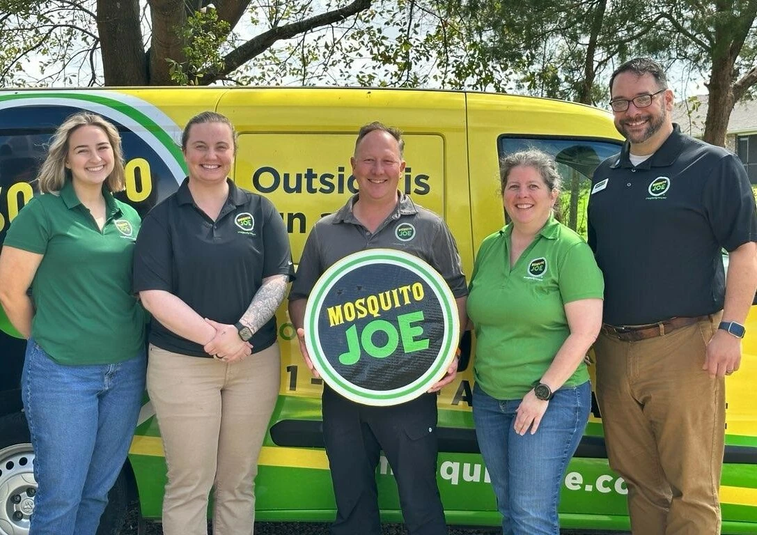 The expert team of Mosquito Joe of Gulf Coast Alabama holding a brand sign standing in front of a brand vehicle.