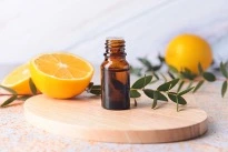 Bottle of lemon eucalyptus oil sitting on top of a cutting board with halved lemons and eucalyptus.